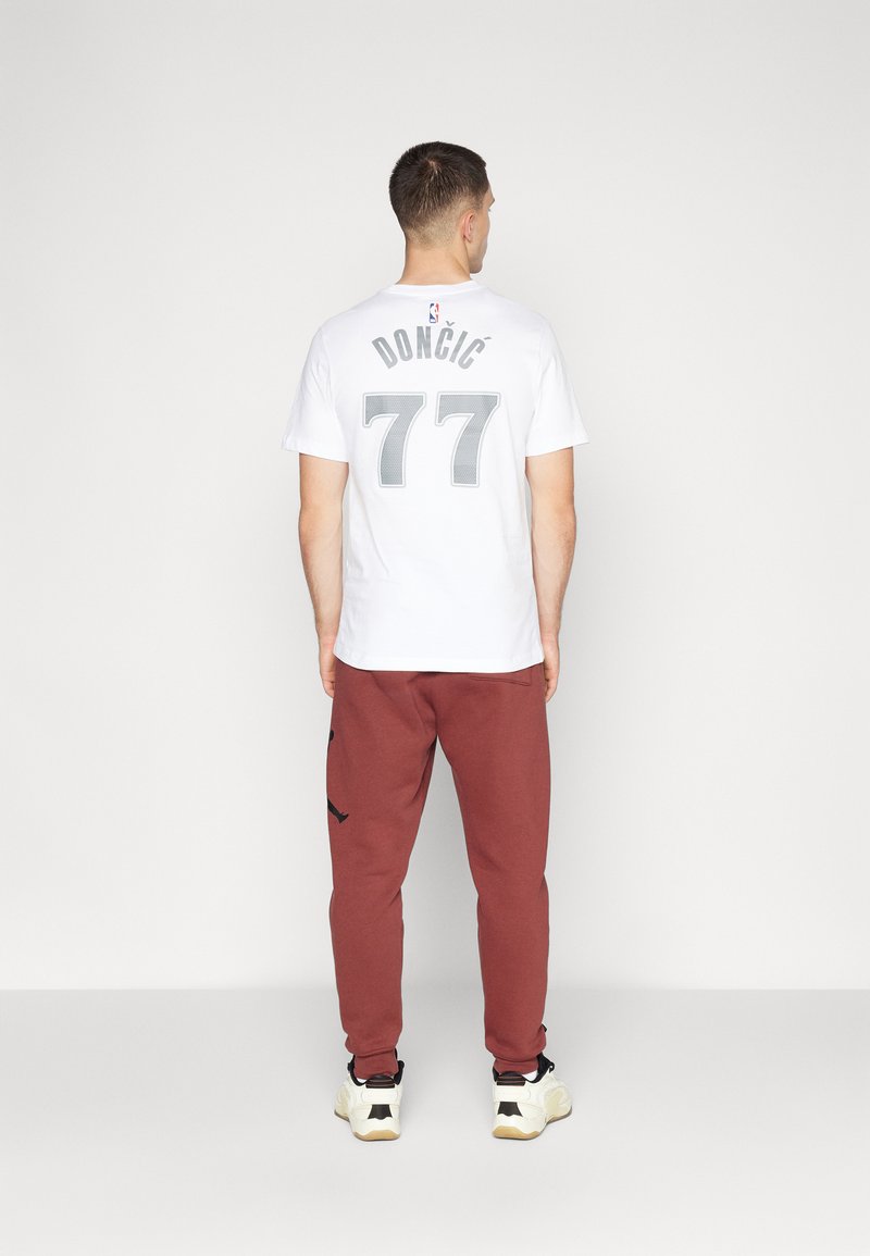 Weißes T-Shirt mit grauem "DONČIĆ"-Text und "77" auf der Rückseite, kombiniert mit burgunderfarbenen Jogginghosen und schwarz-weißen Sneakers.