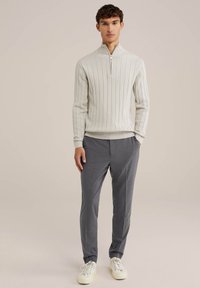 Pulover răsucit de culoare gri deschis, cu guler cu fermoar, asortat cu pantaloni gri închis și adidași albi. Textură netedă și design ajustat.