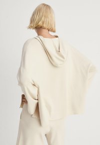 Jasno beżowy, oversize'owy hoodie z kapturem, o luźnym fasonie i miękkiej fakturze. Rękawy i dół mają luźny, swobodny kształt.