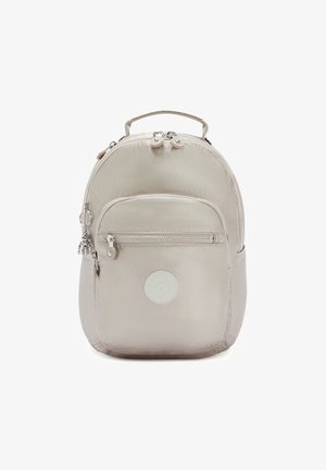 Sac à dos beige en nylon de forme arrondie, avec deux poches zippées et un patch logo à l'avant. Éléments métalliques argentés et poignée supérieure.