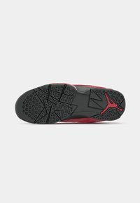 Suela de una zapatilla deportiva roja y negra con patrones de estrellas, agarres circulares y un detalle del logo de Jumpman.