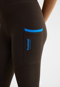 Zwarte geribbelde leggings met een blauwe accentzak en logo. De textuur is glad en de pasvorm is aansluitend.