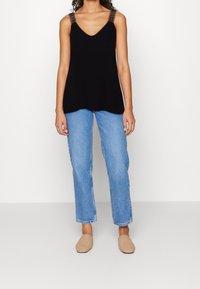 Top senza maniche nero con scollatura a V e spalline decorate, abbinato a jeans azzurri a gamba dritta e scarpe slip-on in paglia beige.