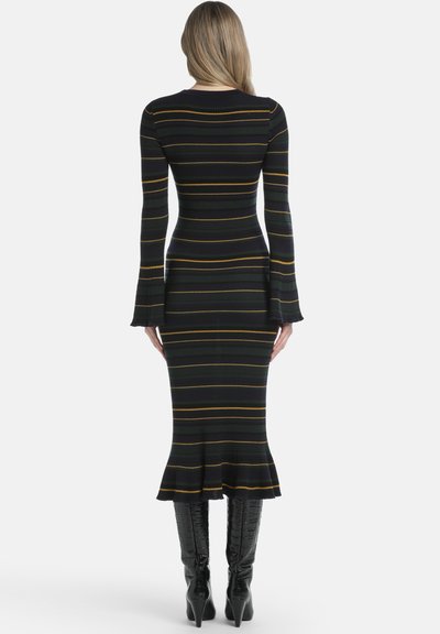 Juoda, raukšlėta megzta suknelė su geltonomis ir žaliomis horizontalinėmis juostomis, ilgomis išplėstomis rankovėmis ir prigludusia siluetu, baigiančia išplėštu kraštu.