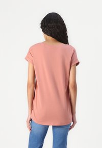 Różowa bawełniana koszulka z krótkimi, podwiniętymi rękawami, luźnym krojem i okrągłym dekoltem; gładka tekstura i dłuższy tylny brzeg.