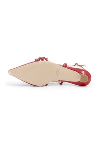 Scarpa con tacco alto in pelle rossa lucida, punta affusolata e cinturino alla caviglia, con una suola beige liscia e un elegante dettaglio con fibbia decorativa.