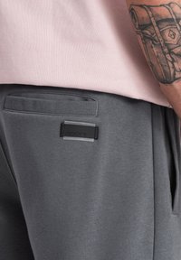 Grå sweatpants med en glat tekstur, der har en syet lomme og en rektangulær sort mærketag på bagbæltet.