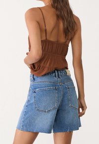 Ruskea teksturoitu toppi ohuilla olkaimilla, yhdistetty vaaleansinisiin farkkushortseihin, joissa on raaka reuna ja kaksi takataskua.