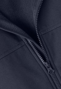 Gros plan d'une veste bleu foncé partiellement dézippée montrant un tissu extérieur lisse, une doublure intérieure en polaire et des dents et curseur de fermeture éclair en métal.