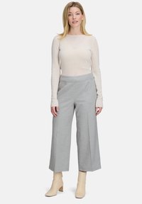 Jasnoszare spodnie szerokie w nogawkach o gładkiej teksturze, w zestawieniu z miękką, beżową bluzką z długim rękawem i beżowymi botkami za kostkę.