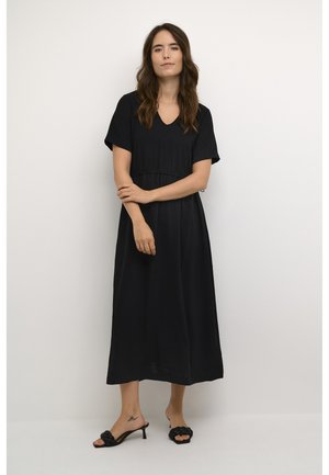 Black maxi dress with short sleeves, V-neckline, cinched waist, and flowing fabric. Worn with braided black heeled sandals.
