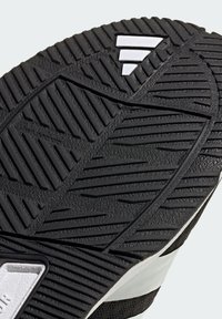 Black shoe sole with textured rubber, featuring a dynamic tread pattern and white accent details. The design emphasizes grip and durability.