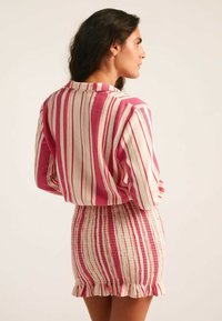 Conjunto de dos piezas a rayas con una combinación de colores en rosa y crema. La parte superior tiene un corte relajado con cuello abotonado; la falda tiene un diseño fruncido y un dobladillo con volantes.