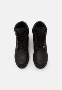 Botas de cuero negras con puntera redondeada, que presentan cordones negros, ojetes de metal y forro de piel sintética. Suela de goma robusta para mayor agarre.