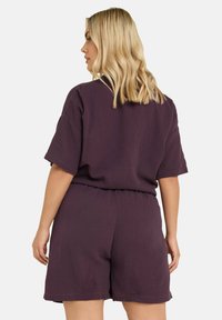 Violetti kudottu asu, jossa on rento istuvuus, lyhyet hihat ja joustava vyötärö, sekä teksturoitu kangaspinta.