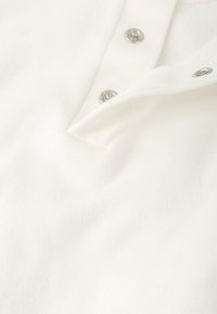 Camisa polo de algodón blanca con un acabado texturizado, que presenta una tapeta con botones a presión plateados y un cuello con muesca.