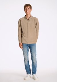 Polo a maniche lunghe beige con texture a coste, dotato di una breve patta. Abbinato a jeans slim-fit azzurri e sneakers bianche.