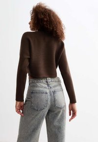 Maglione corto a coste marrone abbinato a jeans a vita alta in denim chiaro. I jeans presentano due tasche posteriori e una vestibilità comoda.