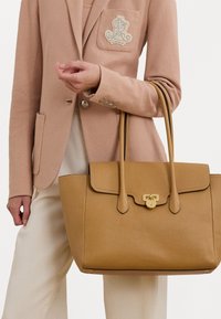 Barna bőr kézi táska, strukturált formával, felső fogantyúkkal, mágneses záródással és fényes arany kiegészítőkkel. Textúrált felület és elegáns design.