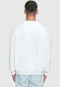 Sweatshirt blanc à coupe décontractée, avec des poignets et une taille côtelés. Tissu doux avec une texture lisse, doté d'épaules tombantes pour plus de confort.