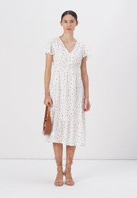 Robes blanches avec des motifs floraux colorés, manches courtes à volants et taille smockée. Comprend une jupe à étages et un décolleté en V.