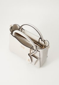 Sac à main blanc texturé avec bordures sombres, doubles poignées et quincaillerie dorée. Comprend un compartiment zippé et une étiquette détachable.