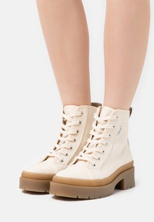 Bottines en toile beige avec une semelle épaisse marron, dotées d'œillets en métal, de lacets et d'un col rembourré pour un confort accru.