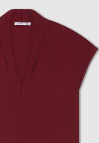 Blusa bordeaux realizzata in tessuto leggero, con scollatura a V e maniche corte, dalla texture liscia e dal design semplice.