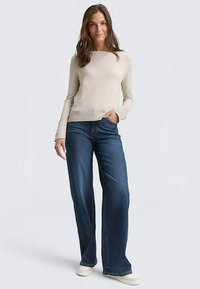 Hellbeiger Pullover mit langen Ärmeln, kombiniert mit dunkelblauen Jeans im Wide-Leg-Stil. Das Outfit wird durch neutrale Slip-On-Schuhe ergänzt.