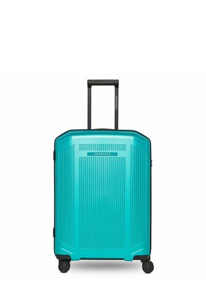 Valigia rigida turchese con scanalature verticali, quattro ruote pivottanti e manico telescopico nero esteso.
