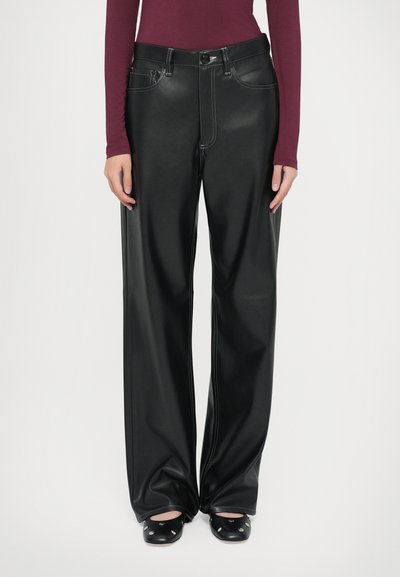 Pantalons larges en simili cuir noir avec des coutures blanches contrastantes, taille haute et poches avant. Associés à des chaussures à talons noires.