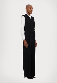 Chaleco negro de doble botonadura sobre una camisa blanca, acompañado de pantalones de pierna ancha. Tejido suave, diseño minimalista y tacones negros de punta.