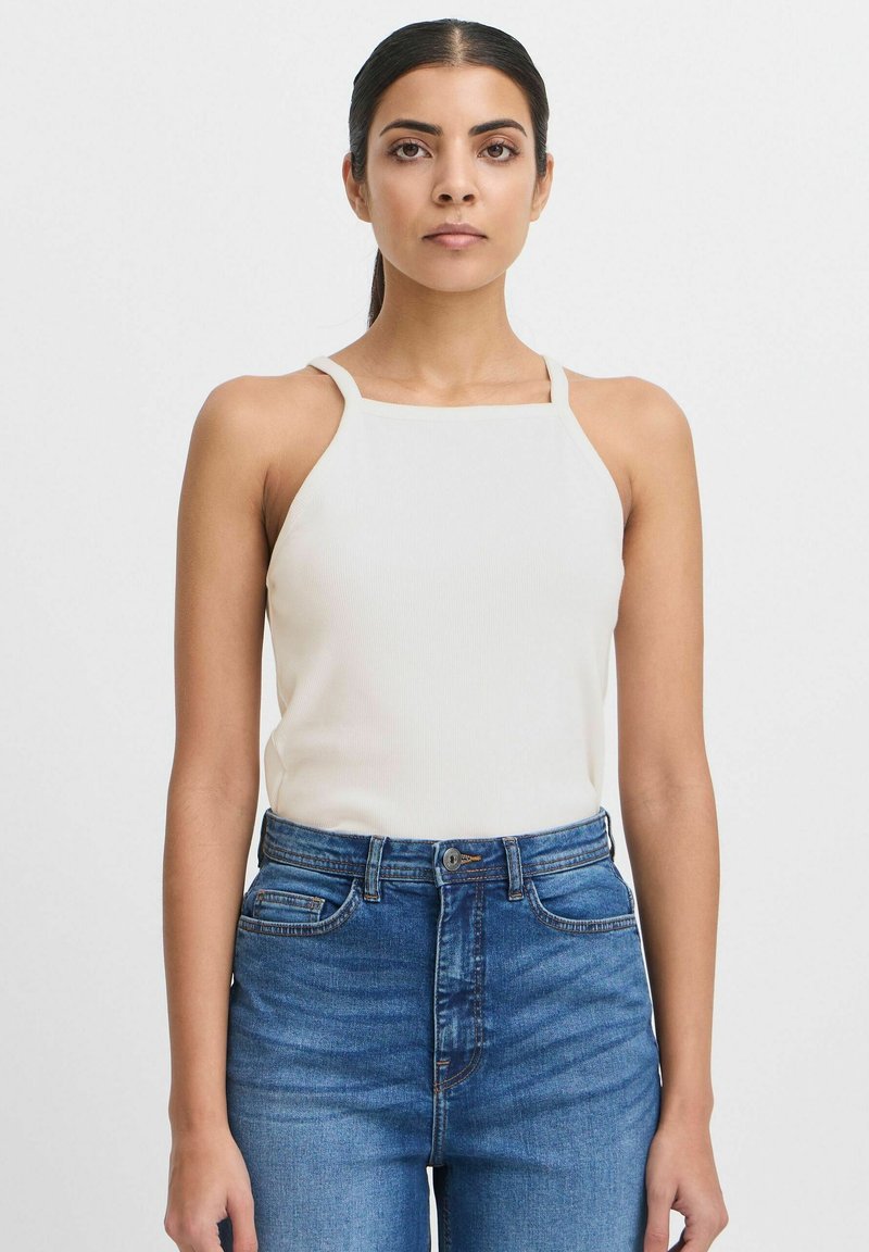 Top halter blanco acanalado con tirantes finos, combinado con jeans de mezclilla azul de cintura alta. El conjunto presenta un diseño ajustado y una textura suave.