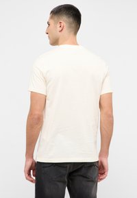Cream short-sleeve T-shirt made from soft cotton, featuring a classic crew neck and a relaxed fit, paired with dark jeans.