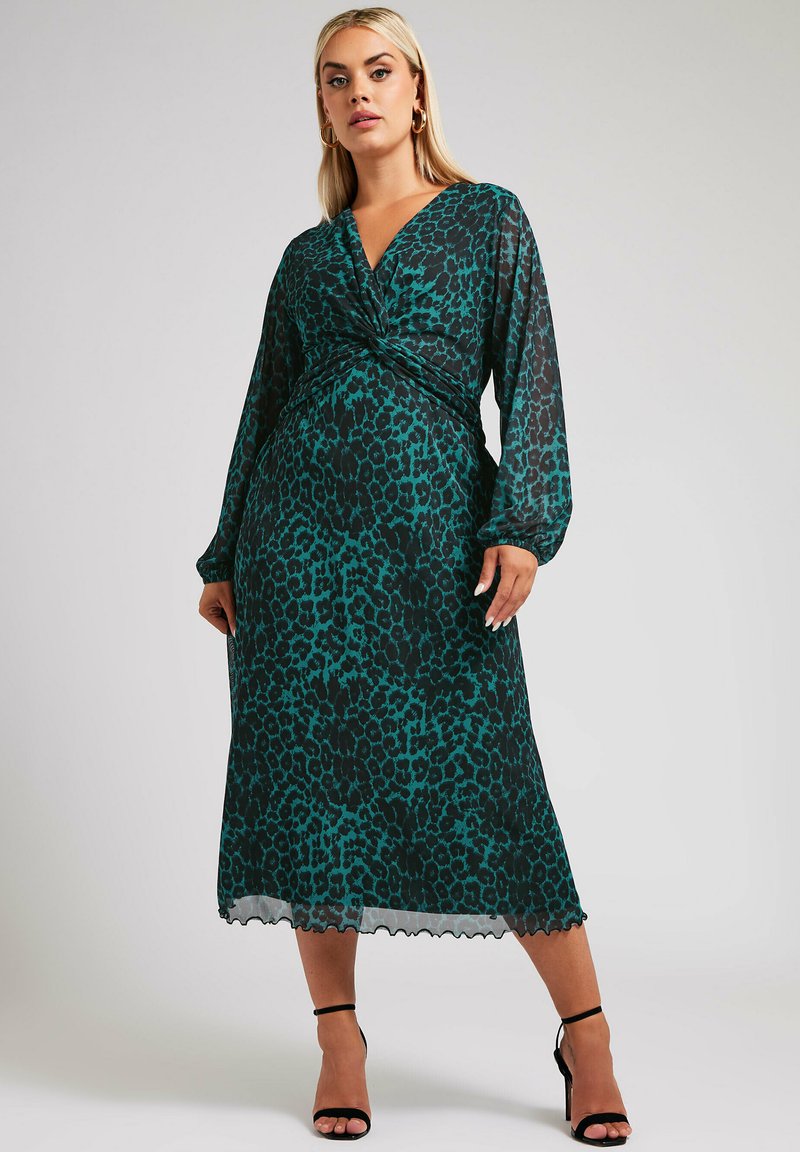 Leopardenmuster Wickelkleid in Türkis und Schwarz, durchsichtige lange Ärmel, knielang mit verdrehter Vorderseite, gewelltem Saum, kombiniert mit schwarzen Riemchen-Heels.