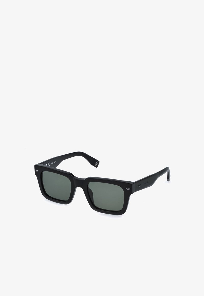 Lunettes de soleil rectangulaires noires avec des verres teintés foncés et des montures épaisses, légèrement inclinées vers la droite sur un fond blanc.