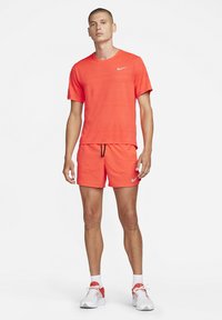 Männliches Sportoutfit mit einem leuchtend orangefarbenen, strukturierten Kurzarmhemd und passenden Shorts, mit einem Nike-Logo und schwarzen Kordelzügen.
