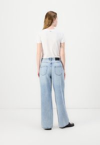 Ανοιχτό μπλε, φαρδιά τζιν παντελόνια με ξεθωριασμένη εμφάνιση και πέντε τσέπες. Συνδυασμένα με μια λευκή μπλούζα κοντομάνικη, με ένα απλό λογότυπο.