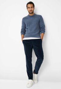 Pantaloni di velluto a coste blu navy abbinati a un maglione blu con texture. L'outfit presenta un colletto rotondo e polsini a coste, completato da sneakers bianche.