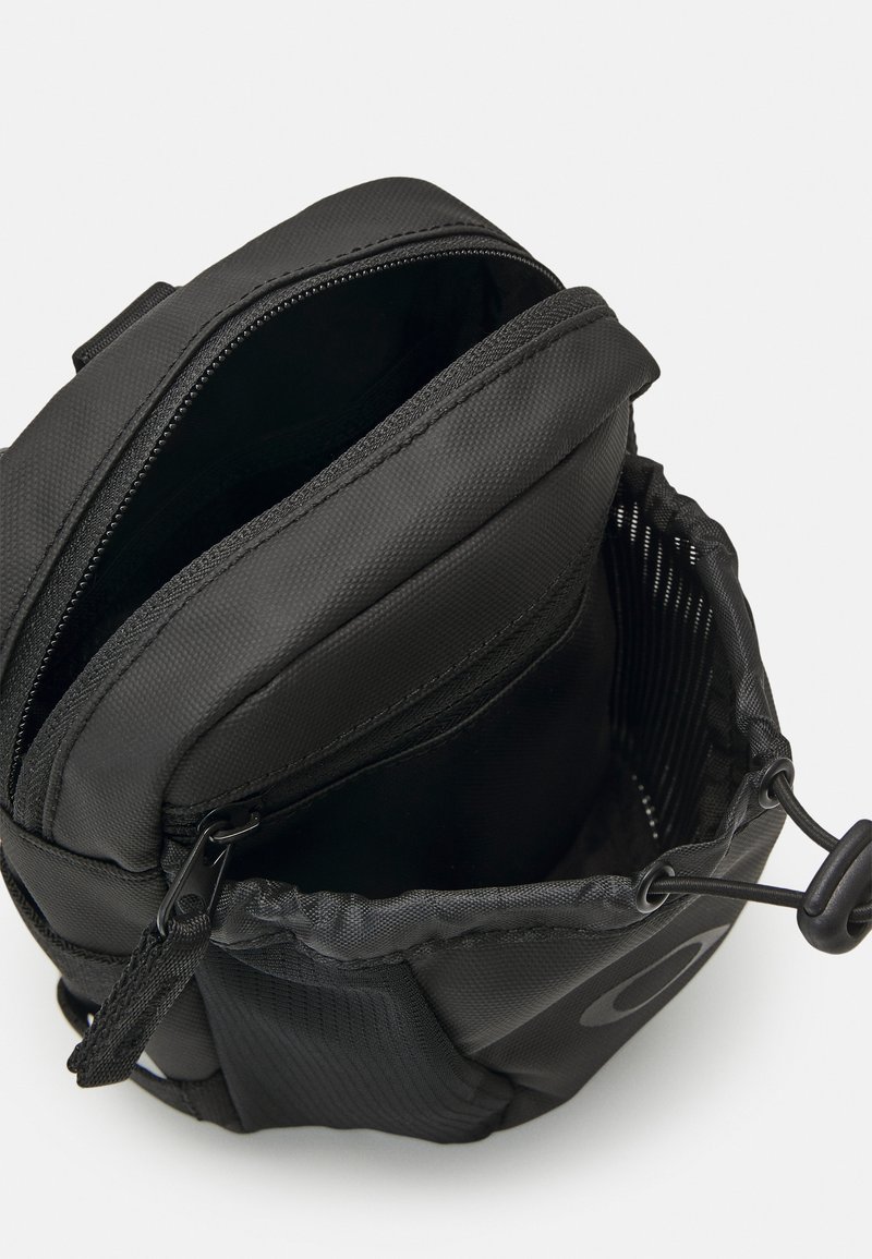 Schwarze Stofftasche mit strukturierter Oberfläche, ausgestattet mit einem Reißverschluss und einem Zugband zur oberen Öffnung. Innen wirkt sie geräumig mit einem einzelnen Fach.