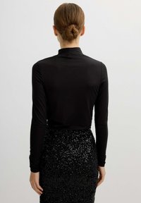 Top negro de manga larga con cuello alto, hecho de un tejido suave, combinado con una falda negra con lentejuelas que resalta una textura brillante y un diseño ajustado.