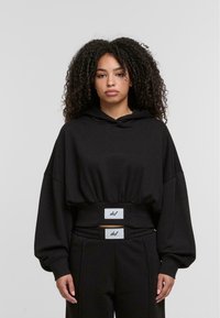Zwarte hoodie met een cropped ontwerp, brede mouwen en een elastische tailleband met merkaccenten. Glad textuur van de stof.