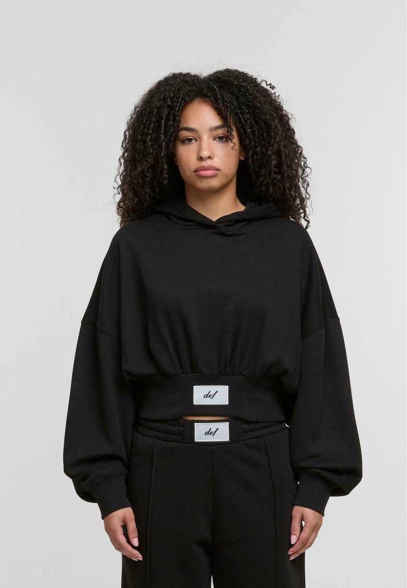 Sort hætte trøje med en cropped design, brede ærmer og elastisk talje med mærkeaccentuer. Glat stofstruktur.