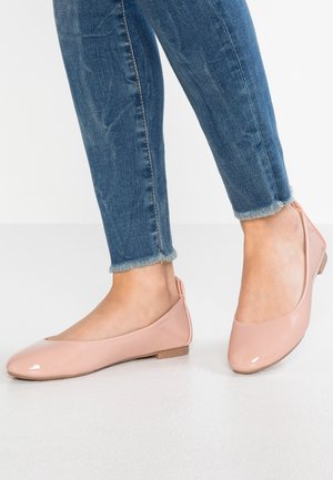 Pieds portant des ballerines en cuir verni rose clair associées à un jean bleu coupé avec des ourlets effilochés.