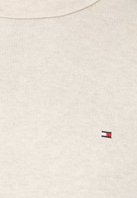 Pull en maille côtelée beige clair avec un petit logo rouge, blanc et bleu sur la poitrine gauche, fabriqué à partir d'un tissu doux et texturé.