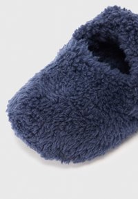 Sötét tengeri kék papucs, puha, bolyhos textilből, lekerekített formával és nyitott felső résszel. A felszíne texturált, bolyhos megjelenéssel rendelkezik.