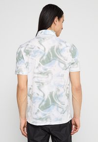 Kurzärmliges Polohemd in Weiß mit blau-grünem abstraktem Muster, einem Kragen und strukturiertem Stoff.