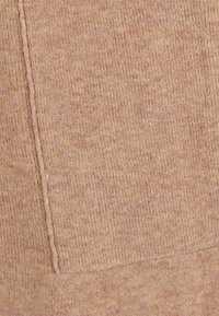 Tessuto in maglia di colore pesco pastello caldo con una superficie testurizzata e una tasca a toppa visibile. Cuciture dettagliate lungo i bordi.