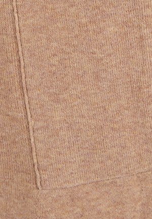 Tessuto in maglia di colore pesco pastello caldo con una superficie testurizzata e una tasca a toppa visibile. Cuciture dettagliate lungo i bordi.