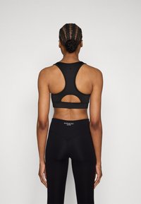 Czarny sportowy biustonosz z paskiem typu racerback i wycięciem. W zestawie z czarnymi legginsami o wysokim stanie, z logo na pasku.